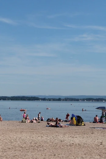 Badestrand Mardorf Strand mit Sonnenbadenden und Schirmen am Steinhuder Meer, sanfte Hügel im Hintergrund.