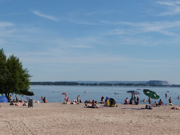 Badestrand Mardorf Strand mit Sonnenbadenden und Schirmen am Steinhuder Meer, sanfte Hügel im Hintergrund.