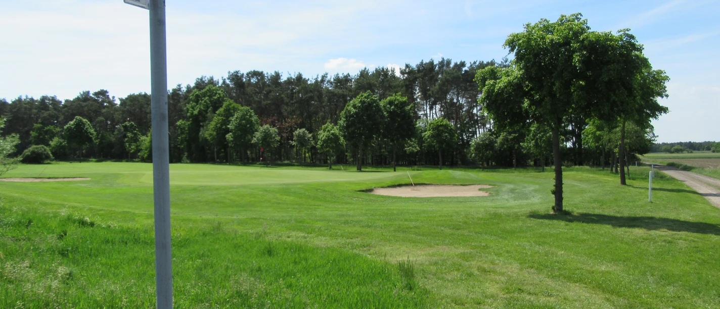 Golfpfad Weitläufiger Golfpfad mit gepflegtem Rasen, umgeben von Bäumen unter klarem blauem Himmel.
