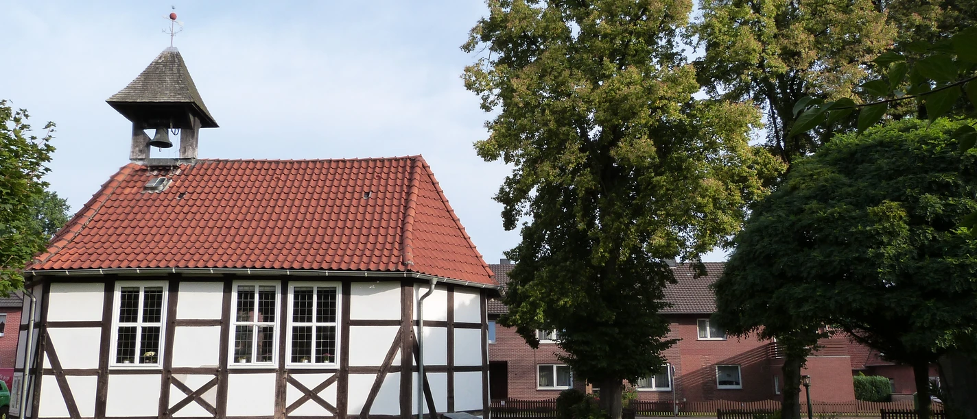 Kirche Mardorf Eine kleine Fachwerkkirche mit roten Ziegeldach neben einem grünen Baum im Dorfzentrum.