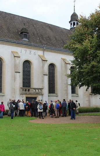 Eine Gruppe von Menschen versammelt sich vor einer historischen Kirche mit dem Baujahr 1736.