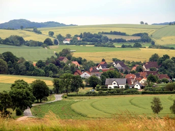 Blick auf Heidelbeck mit Fachwerkhäusern, umgeben von sanften Hügeln und weitläufigen Feldern.