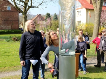 Wasserstrudel Eine Frau und ein Mann betrachten fasziniert einen Wassertornado in einer transparenten Röhre im Freien.