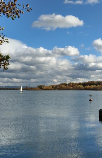 Herbstliche Landschaft am Lippesee mit Segelboot, Wolkenhimmel und Ufer im Vordergrund.