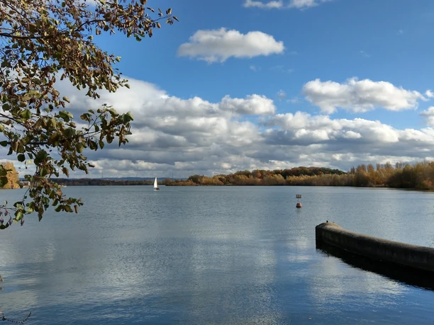 Blick über den Lippesee Herbstliche Landschaft am Lippesee mit Segelboot, Wolkenhimmel und Ufer im Vordergrund.