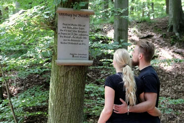 Infotafel zur Uffoburg (hitorische Wallanlage) Infotafel zur Uffoburg im Wald, mit zwei Menschen, die den Text aufmerksam lesen.