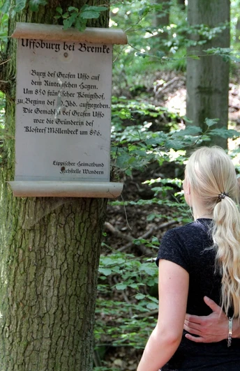 Infotafel zur Uffoburg (hitorische Wallanlage) Infotafel zur Uffoburg im Wald, mit zwei Menschen, die den Text aufmerksam lesen.
