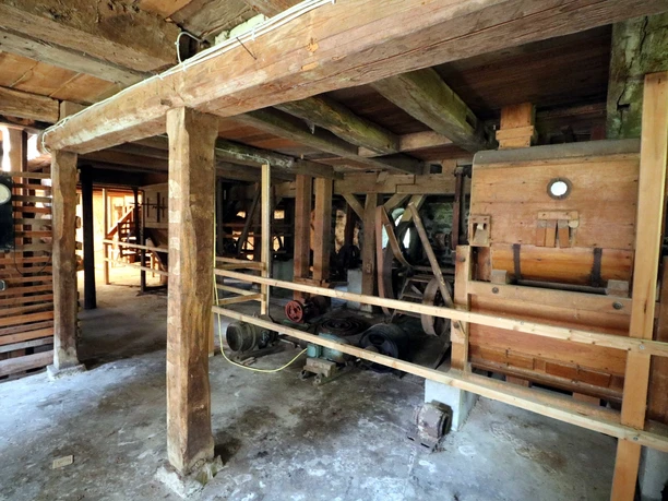 Historische Holzkonstruktion in altem Gebäude, mit massiven Balken, Maschinen und technischen Details.