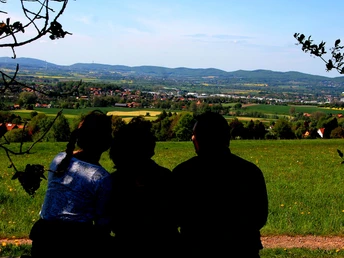 Aussichtsreich ins Weserbergland Drei Personen blicken auf das grüne Weserbergland mit Hügeln und Dörfern unter einem klaren Himmel.