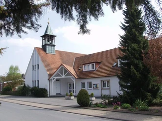 Oesterweg Eine weiße Kirche mit einem kleinen Turm, umgeben von Bäumen, unter einem strahlend blauen Himmel.