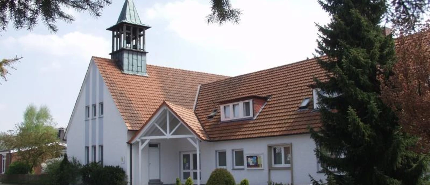 Oesterweg Eine weiße Kirche mit einem kleinen Turm, umgeben von Bäumen, unter einem strahlend blauen Himmel.