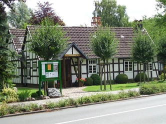 Schwarzes Fachwerkhaus mit weißen Wänden, umgeben von gepflegtem Garten und Informationstafel.