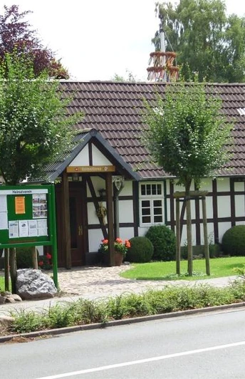 Heimatmuseum Oesterweg Schwarzes Fachwerkhaus mit weißen Wänden, umgeben von gepflegtem Garten und Informationstafel.
