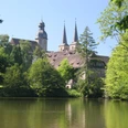 Abteikirche Blick auf die Abteikirche mit zwei spitzen Türmen, umgeben von grünen Bäumen und einem ruhigen See.