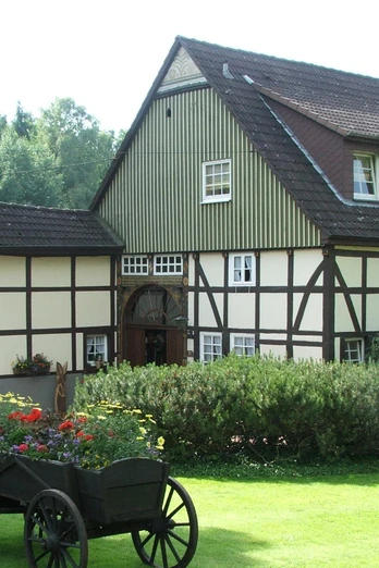 Haus Berkenkamp Fachwerkhaus mit Satteldach, umgeben von grünem Garten und Blumenkarren im Vordergrund.