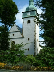 Kath. Pfarrkirche St. Jakobus Historische Kirche mit grünem Turm und Uhr, umgeben von Bäumen und bunten Blumenbeeten.
