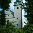 Kath. Pfarrkirche St. Jakobus Historische Kirche mit grünem Turm und Uhr, umgeben von Bäumen und bunten Blumenbeeten.