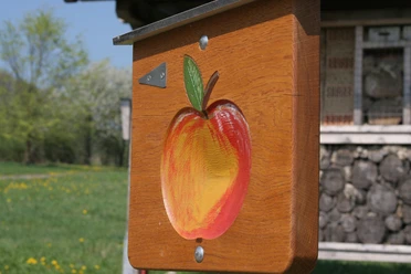 Der Apfel weist den Weg Ein Holzschild mit einem bunten Apfel weist auf einen Wanderweg in ländlicher Umgebung hin.