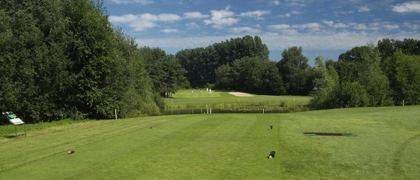 Golfplatz Peckeloh Golfplatz im Grünen mit weitläufigem Fairway, umgeben von Bäumen und blauem Himmel im Hintergrund.