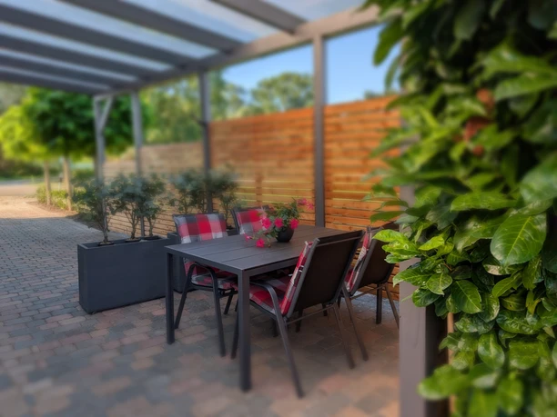 Überdachte Terrasse mit Tisch, vier Stühlen, Pflanzen und Sichtschutz aus Holz.
