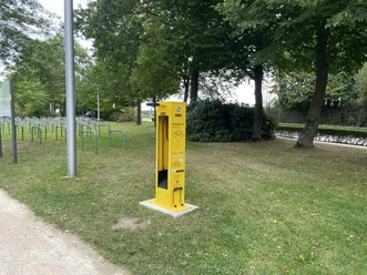 Gelbe ADAC-Radservice-Station auf einer Wiese neben Fahrradständern und Bäumen.