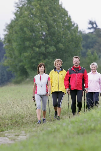 Nordic Walking auf dem Gesundheits - & Fitness-Parcours Vier Personen beim Nordic Walking auf einem Fitness-Parcours, umgeben von Wiesen und Bäumen.