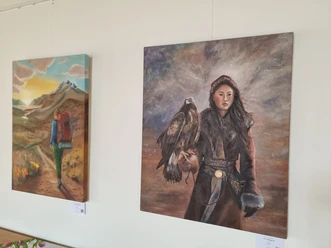 Gemälde einer Frau mit einem Adler auf dem Arm. Dahinter ein zweites Bild mit einer Wanderin.