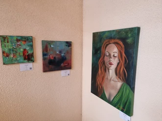 Drei Gemälde an einer Wand; links abstrakte Kunst, rechts Porträt einer Frau mit roten Haaren in grüner Bluse.