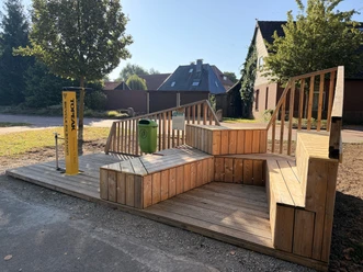 Gelbe Fahrrad-Reparaturstation neben einer Holzplattform mit Sitzbänken im Freien.