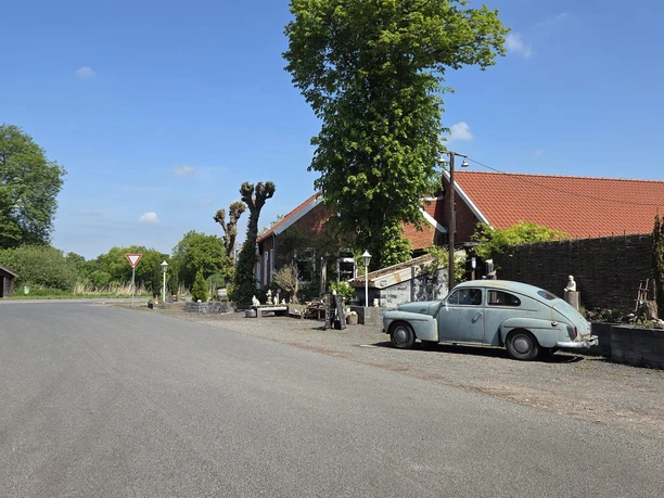 Pausenstation Marienheil mit rotem Dach, altem VW Käfer und Bäumen an einer Landstraße.