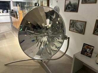 A mirrored solar grill in the museum, surrounded by display cases and pictures depicting dining culture