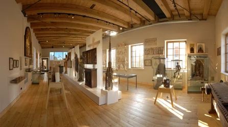 Ein heller Museumsraum mit Holzdecke, Exponaten in Vitrinen und Skulpturen auf einem Podest.