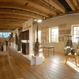 Ein heller Museumsraum mit Holzdecke, Exponaten in Vitrinen und Skulpturen auf einem Podest.