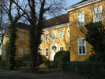 Haus Münte Gelbes, historisches Gebäude mit weißen Fenstern, umgeben von Bäumen und einem Zaun im Vordergrund.