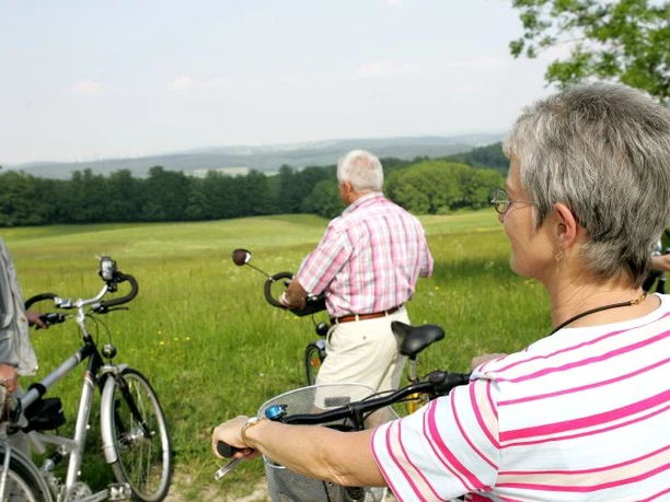 Bad Driburger Radroute, Tour 1 Drei Senioren genießen eine Radtour durch eine grüne, weitläufige Wiesenlandschaft bei sonnigem Wetter.