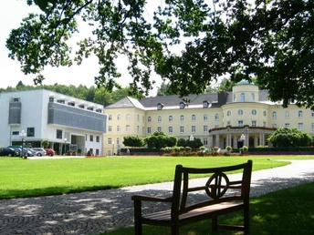 Park Bad Hermannsborn - Bad Driburger Ortsteil Historisches Kurhaus im Park Bad Hermannsborn mit umliegender grüner Rasenfläche und Sitzbank.