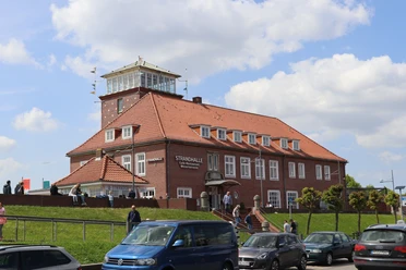 Strandhalle Bremerhaven mit rotem Ziegeldach auf dem Deich, davor Straße und Autos.