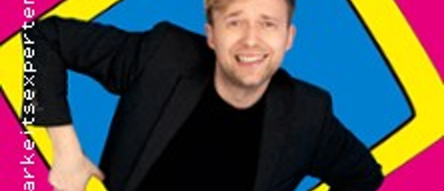 Marc Weide lehnt lachend durch einen gelben Rahmen vor pinkem Hintergrund