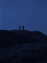 Zwei Personen stehen in weiter Ferne auf einer Felslandschaft bei einsetzender Dämmerung.