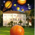 Ein großes, historisches Gebäude wird von einer fantasievollen Darstellung des Sonnensystems überragt.