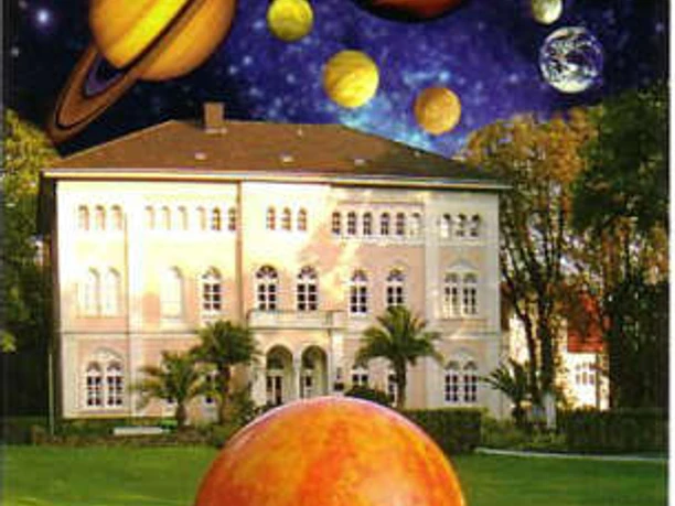 "Der Planetenweg" Bad Lippspringe Ein großes, historisches Gebäude wird von einer fantasievollen Darstellung des Sonnensystems überragt.