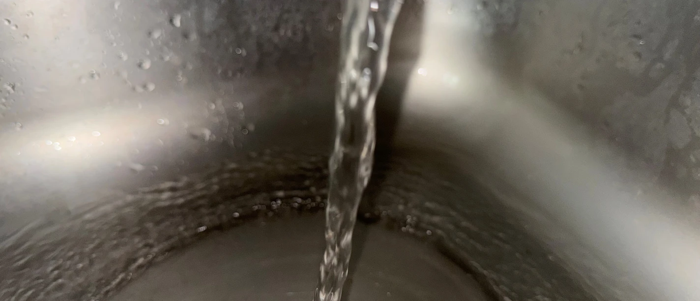 Wasserstrahl läuft in ein Edelstahlbecken eines Trinkwasserbrunnens.