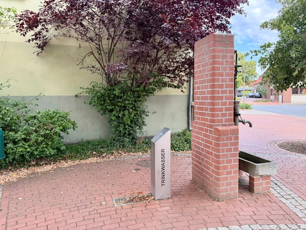 Trinkwasserbrunnen mit Backsteinsäule und Hinweisschild auf dem Marktplatz in Steyerberg.
