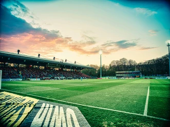 Soccer field at Höhenberg Stadium with a packed stands at sunset