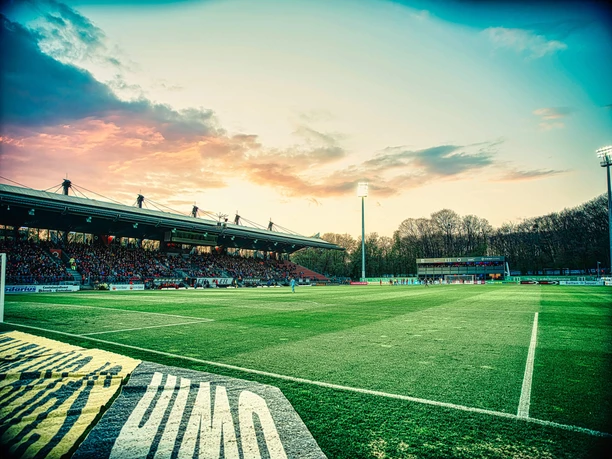 Fußballfeld im Stadion Höhenberg mit voller Tribüne bei Sonnenuntergang