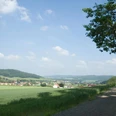 Eine weite, grüne Landschaft im Eggetal mit einem Kiesweg und vereinzelten Häusern unter blauem Himmel.