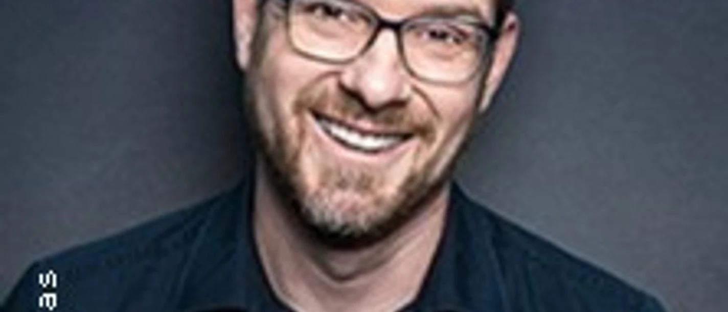 Porträt von Sascha Thamm, lächelnd mit Brille vor dunklem Hintergrund