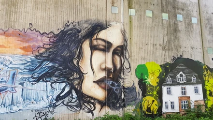 Graffiti an Betonwand mit Frauenporträt, Wellen und gemaltem Haus