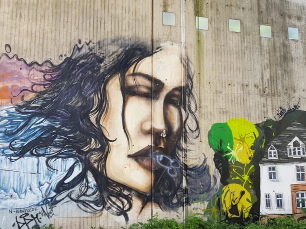 Graffiti an Betonwand mit Frauenporträt, Wellen und gemaltem Haus