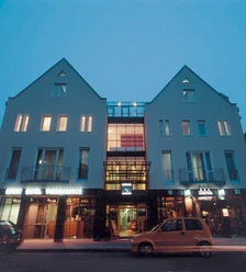 Außenansicht Sporthotel Wiedenbrück Moderne, beleuchtete Hotel-Fassade bei Dämmerung, mit großen Fenstern und Glasüberdachung.